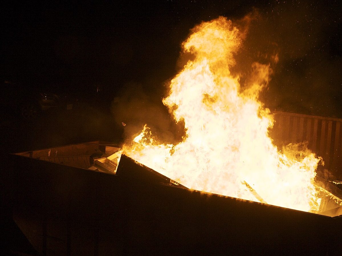 A dumpster engulfed in huge flames at night.